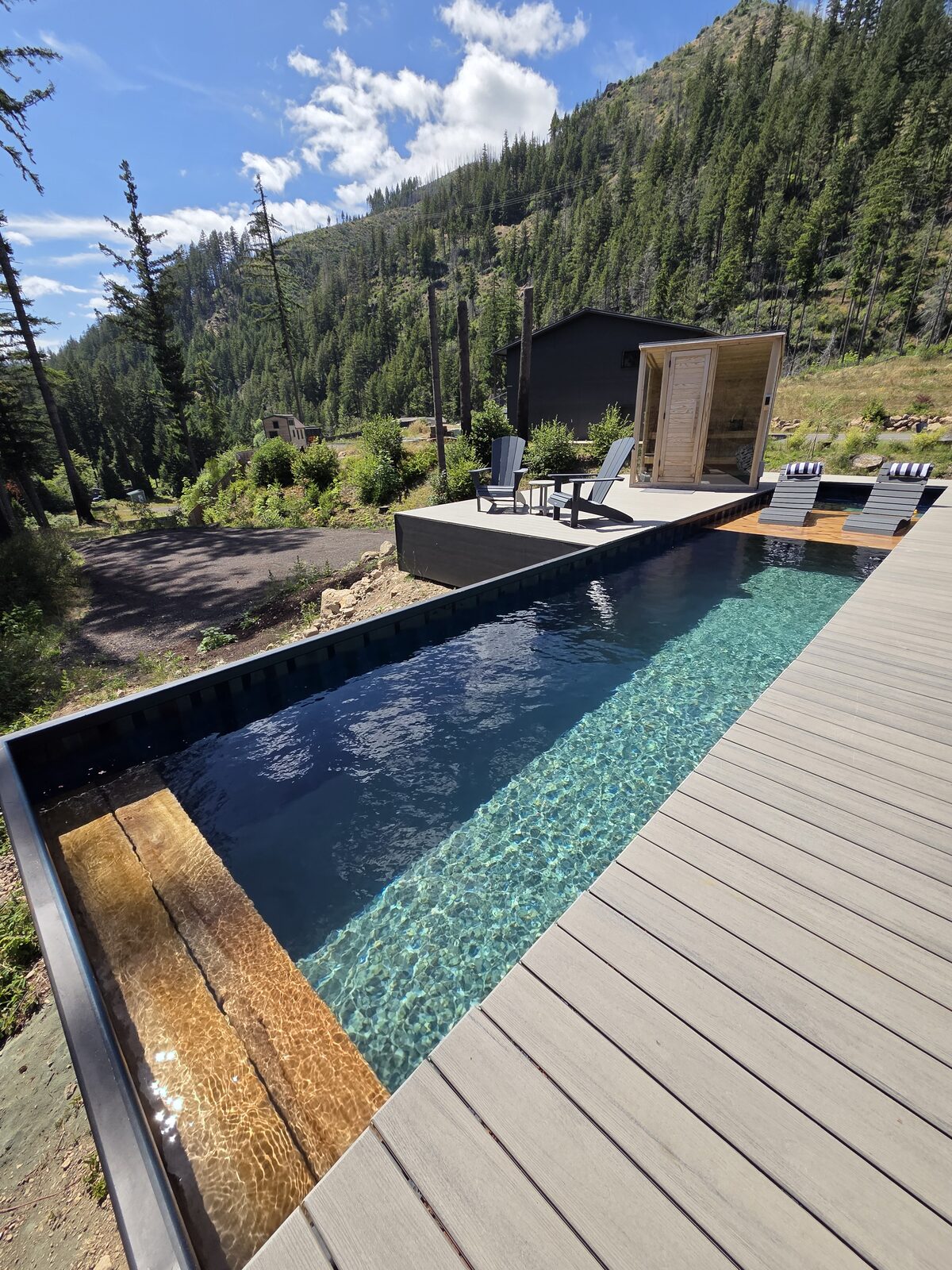 Container pool with deck loungers and cedar sauna, forested hillside behind