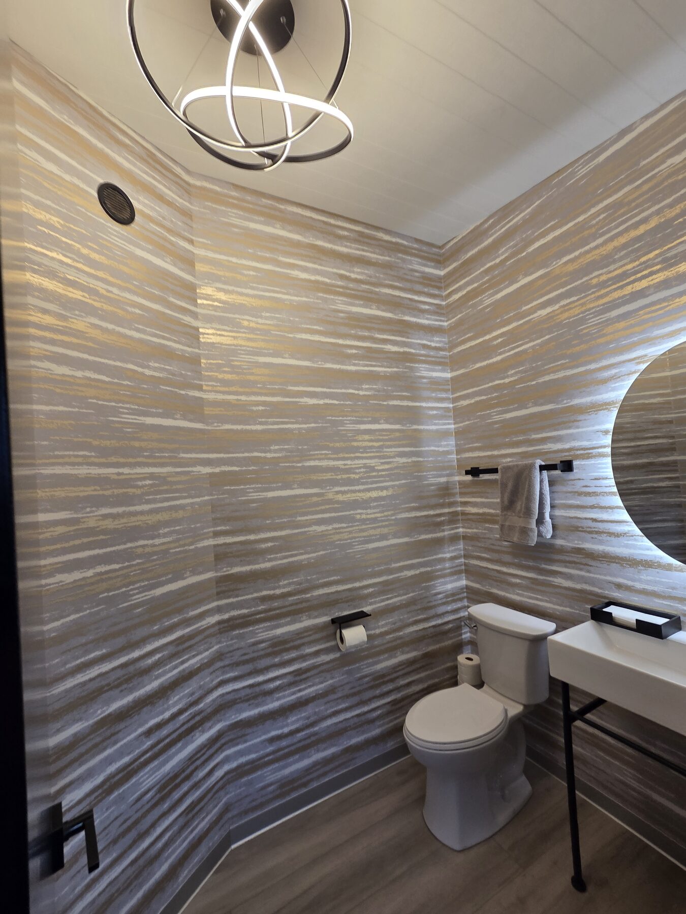 Powder room with artistic chandelier and gold wallpaper